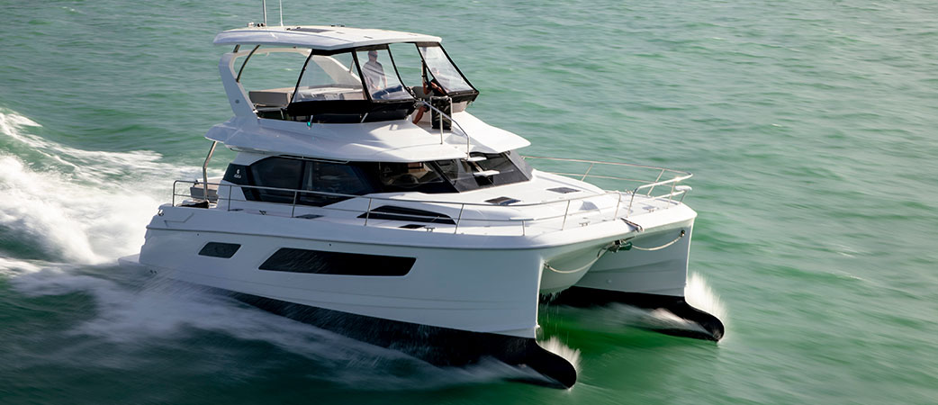 Catamarán a motor Aquila 44 Yacht navegando a toda velocidad en aguas abiertas, con el sol brillando en el casco y las olas rompiendo a su paso.